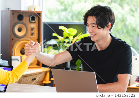 ベンチャー企業のオフィスで力強く手を握り合い協力を誓う若いビジネスパーソン ベンチャー企業のオフィスで力強く手を握り合い協力を誓う若いビジネスパーソン 142158522