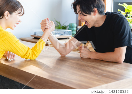 オフィスのデスクで白熱した表情で力比べをする男女 オフィスのデスクで白熱した表情で力比べをする男女 142158525