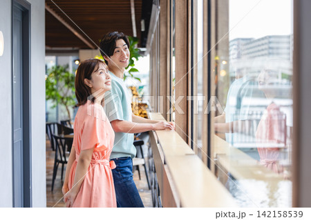 おしゃれなカフェの廊下で外を眺めながら会話を楽しむ若い男女 おしゃれなカフェの廊下で外を眺めながら会話を楽しむ若い男女 142158539