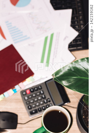 Calm workspace with documents, calculator, coffee, and leafy green plant Calm workspace with documents, calculator, coffee, and leafy green plant 142159162