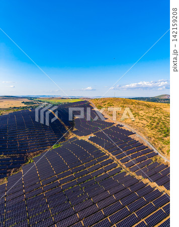 Solar panels cover a large area on a hillside under a clear blue sky during the daytime in a rural location Solar panels cover a large area on a hillside under a clear blue sky during the daytime in a rural location 142159208