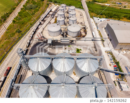 Cylindrical grain storage structures stand near railway tracks in an industrial area on a sunny day Cylindrical grain storage structures stand near railway tracks in an industrial area on a sunny day 142159262