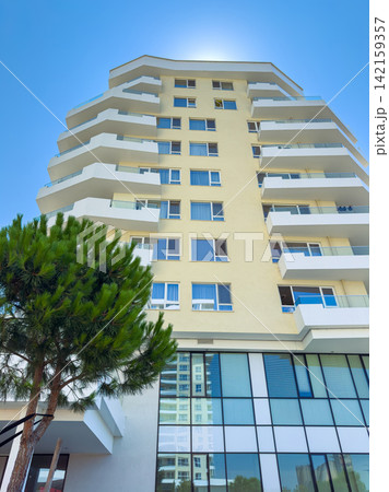 View of a tall building with multiple balconies seen from below during a sunny day in a residential area View of a tall building with multiple balconies seen from below during a sunny day in a residential area 142159357
