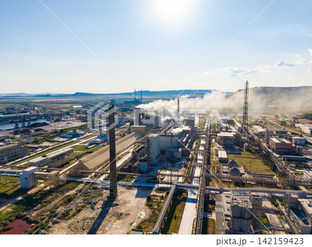 Industrial complex with smoke rising in the sky during daytime near a river Industrial complex with smoke rising in the sky during daytime near a river 142159423