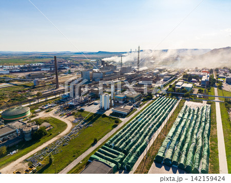Industrial area with factories, smoke, and storage facilities in a rural setting during daytime Industrial area with factories, smoke, and storage facilities in a rural setting during daytime 142159424