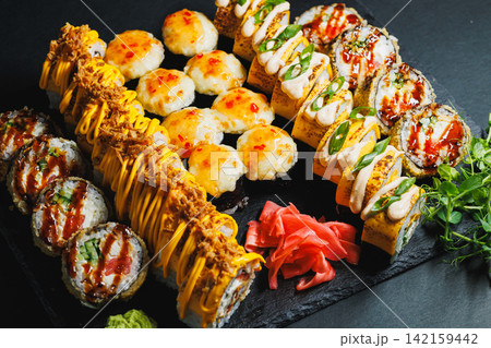Sushi platter with various types of rolls and garnishes displayed on a dark stone serving board 142159442