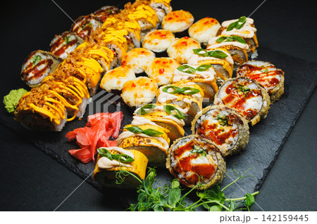Sushi platter served on a dark stone tray with various rolls and sauces in a dining setting 142159445