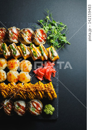 Sushi served on a black stone platter with sauces and garnishes arranged on a table 142159483