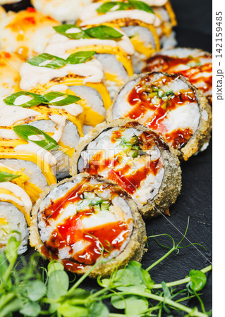 Sushi rolls on a black plate with sauces and garnish arranged in a colorful display at a restaurant setting 142159485