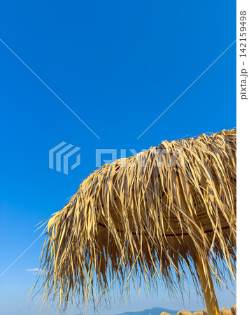 Sunshade made of straw stands against blue sky during daytime 142159498