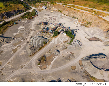 Construction site with machinery and quarry at work during daytime in an open area surrounded by hills and greenery 142159571