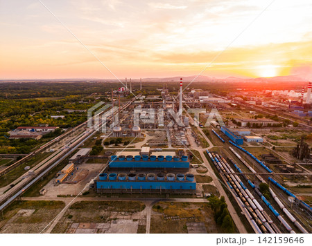 Factory complex in the evening during sunset with trains passing and a scenic landscape surrounding the area Factory complex in the evening during sunset with trains passing and a scenic landscape surrounding the area 142159646