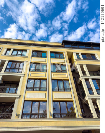 Modern building with large windows under a blue sky with fluffy clouds in an urban area during daytime Modern building with large windows under a blue sky with fluffy clouds in an urban area during daytime 142159691
