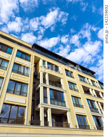 Building shows modern architecture with large windows and balconies under a blue sky with clouds in an urban area during daytime Building shows modern architecture with large windows and balconies under a blue sky with clouds in an urban area during daytime 142159692