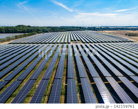 Solar panels cover a large area in an open field during the day with a clear sky and some clouds in the background Solar panels cover a large area in an open field during the day with a clear sky and some clouds in the background 142159761