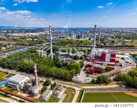 Factory site with large chimneys and green areas located near a city during daytime Factory site with large chimneys and green areas located near a city during daytime 142159772