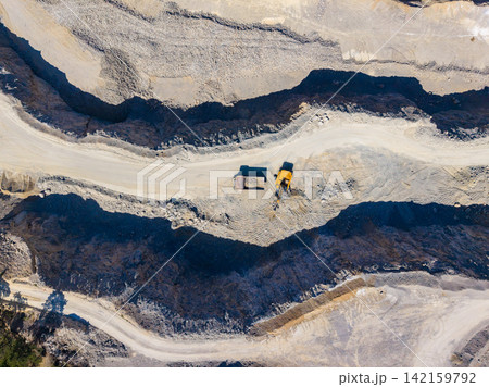 Work takes place at a mining site with heavy machinery moving earth and rock among deep excavations during daytime Work takes place at a mining site with heavy machinery moving earth and rock among deep excavations during daytime 142159792