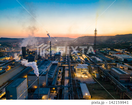 Industrial area with factories and smoke in the evening sky near a mountain range Industrial area with factories and smoke in the evening sky near a mountain range 142159941