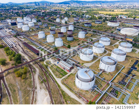 Industrial storage facility with multiple tanks and pipelines near a city landscape in daylight 142159997