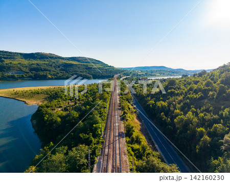 Tracks run beside water and hills under a clear sky in a green landscape Tracks run beside water and hills under a clear sky in a green landscape 142160230