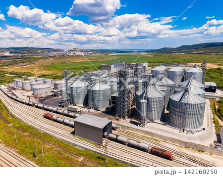Grain storage facility with many silos located by train tracks in a rural area under a bright sky Grain storage facility with many silos located by train tracks in a rural area under a bright sky 142160250