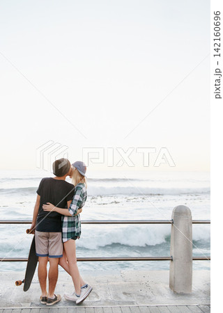 Couple, kiss and romance on beach for date with mockup space, adventure and skateboard on promenade. Skater, people and hugging on boardwalk for bonding, embrace and outdoor travel with sea waves 142160696