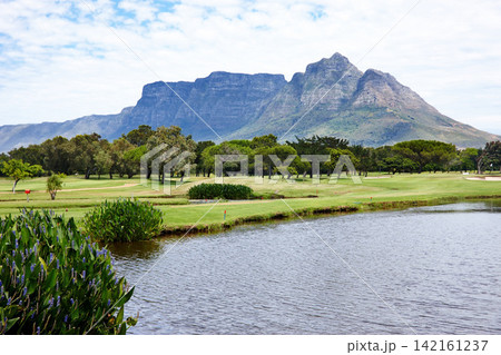 Mountain, landscape and water with grass at golf course in summer on holiday or vacation. Calm, morning and lake with turf field for sport in woods, forest or nature of park with trees and plants 142161237