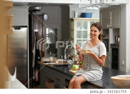 Happy, woman and sitting on table top in kitchen for nutrition, hungry and eating in apartment for diet. Nutritionist, diet and wellness in house for cookbook, organic and vegan recipes in home Happy, woman and sitting on table top in kitchen for nutrition, hungry and eating in apartment for diet. Nutritionist, diet and wellness in house for cookbook, organic and vegan recipes in home 142161755