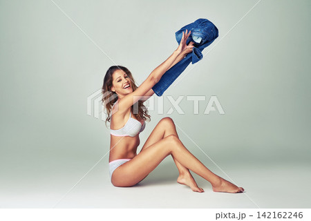 Fashion, smile and underwear with woman undressing in studio on gray background for casual style. Denim jeans, model and trendy with portrait of happy young person throwing pants in excitement 142162246