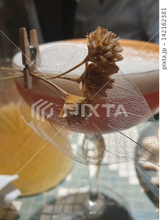 An elegant alcoholic cocktail with foam, decorated with a skeletonized leaf and dried flowers on a wooden clothespin An elegant alcoholic cocktail with foam, decorated with a skeletonized leaf and dried flowers on a wooden clothespin 142162381