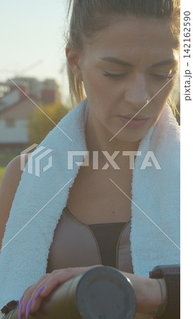 Vertical video. Woman tracking her running progress with a smartwatch in the city stadium. Vertical video. Woman tracking her running progress with a smartwatch in the city stadium. 142162590