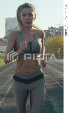 Vertical video. Pretty sporty woman running in the sports stadium. Fitness, workout and technology. 142162658