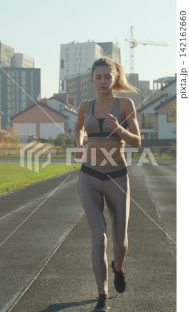 Vertical video. Pretty sporty woman running in the sports stadium. Fitness, workout and technology. Vertical video. Pretty sporty woman running in the sports stadium. Fitness, workout and technology. 142162660