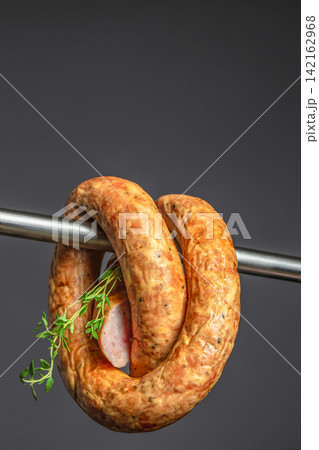 Sausage coil hanging on a metal rod with fresh herbs, showcasing a close-up view of the meat texture and color against a dark background. space for text 142162968