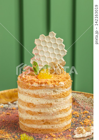 Layered honey cake with decorative honeycomb and edible flowers on a golden plate against a green background, showcasing intricate dessert design and presentation Layered honey cake with decorative honeycomb and edible flowers on a golden plate against a green background, showcasing intricate dessert design and presentation 142163019