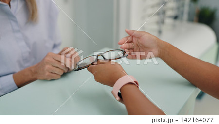 Glasses, frame and hands of patient at counter by employee in clinic for vision, prescription or eye care. Optometrist, healthcare or lens or health for eyes, glaucoma and ocular diseases or eyesight Glasses, frame and hands of patient at counter by employee in clinic for vision, prescription or eye care. Optometrist, healthcare or lens or health for eyes, glaucoma and ocular diseases or eyesight 142164077