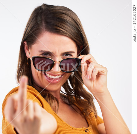 Studio, portrait and woman with rude middle finger, glasses and comedy expression. Face, smile and rebel from female model with hand gesture, comedy and silly joke with attitude and emoji and curse 142165027
