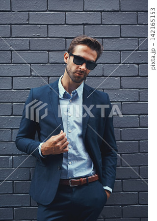 Male model, wall and fashion with suit or confident for clothing, sunglasses or trendy and cool. Businessman, backdrop and stylish or formal for career with corporate, lawyer with hands in Chicago 142165153