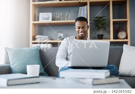 Man, typing and laptop in home on couch, networking and social media for online streaming in living room. Happy, research and technology on website, remote work and internet blog in apartment 142165582