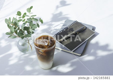 自然光の差し込むデスクとアイスカフェラテ、ノートとユーカリ 自然光の差し込むデスクとアイスカフェラテ、ノートとユーカリ 142165881
