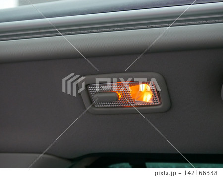 Interior ceiling light turned on in car cabin. Overhead lamp illuminating vehicle upholstery. Automotive lighting system detail for safety and comfort during nighttime drive or travel. 142166338