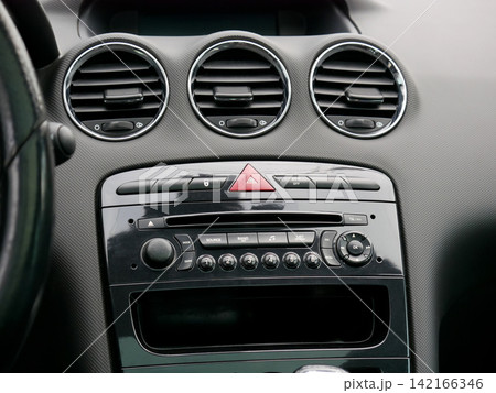 Car interior dashboard showing the center console and air vent. Modern vehicle cockpit design details. Automobile control panel with radio interface, hazard button and climate control ventilation. 142166346
