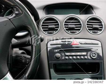 Interior view of modern car dashboard with leather steering wheel. Automotive cabin detail showing air vents and center console audio system. Transport travel and vehicle technology. Interior view of modern car dashboard with leather steering wheel. Automotive cabin detail showing air vents and center console audio system. Transport travel and vehicle technology. 142166347
