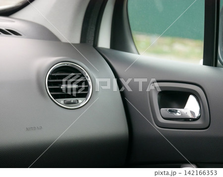 Car interior with air vent and door handle. Close up shot of vehicle dashboard. Automotive design detail and modern transport comfort concept. Safety system with airbag sign included. Car interior with air vent and door handle. Close up shot of vehicle dashboard. Automotive design detail and modern transport comfort concept. Safety system with airbag sign included. 142166353