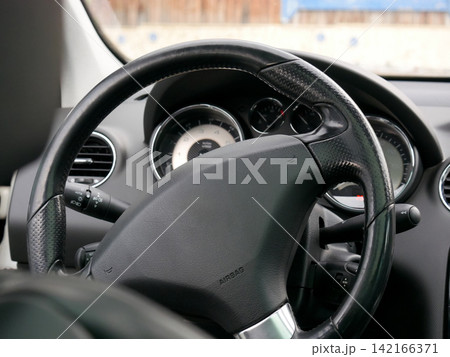 Steering wheel inside modern car interior view. Dashboard with speedometer and tachometer visible. Vehicle control system and transport driver cabin concept for automotive industry. Steering wheel inside modern car interior view. Dashboard with speedometer and tachometer visible. Vehicle control system and transport driver cabin concept for automotive industry. 142166371