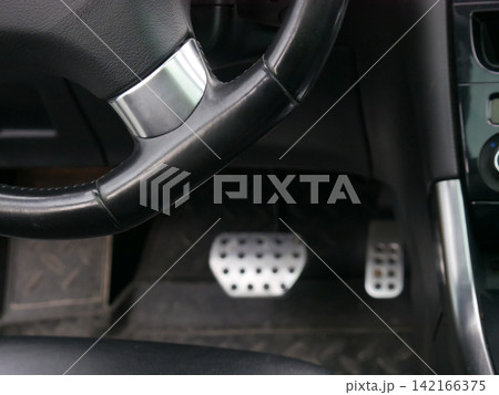 Interior of modern vehicle focusing on steering wheel and metal pedals. Driver view from inside car cockpit. Concept of automotive transportation, driving experience and motor vehicle control. Interior of modern vehicle focusing on steering wheel and metal pedals. Driver view from inside car cockpit. Concept of automotive transportation, driving experience and motor vehicle control. 142166375