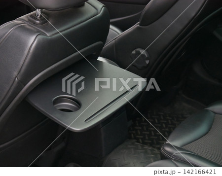 Foldable tray table on back of car seat. Passenger seat accessory with cup holder for travel. Automotive interior feature for convenience of backseat passenger during road trip. 142166421