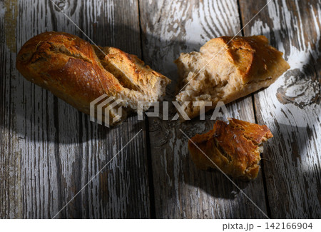 Freshly baked bread resting on rustic wooden table, showcasing its golden crust and soft interior Freshly baked bread resting on rustic wooden table, showcasing its golden crust and soft interior 142166904