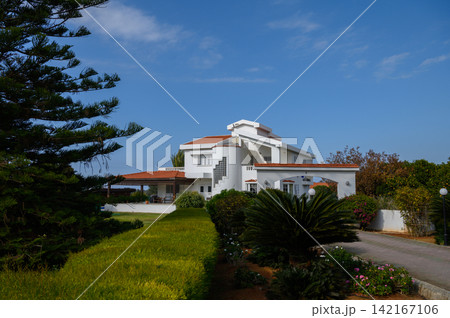 Serene white villa nestled among lush greenery under a vibrant blue sky 142167106