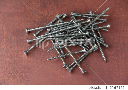 Scattered metal screws create an artistic display on a wooden surface Scattered metal screws create an artistic display on a wooden surface 142167131